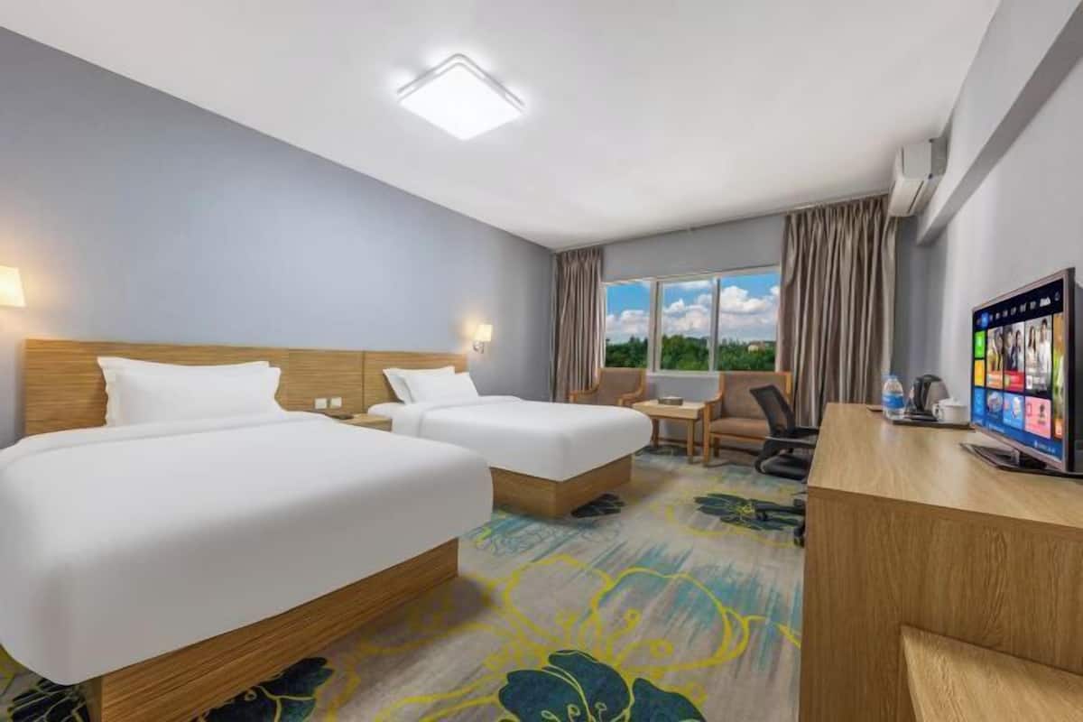 A hotel room with two beds, a desk, a TV, and a window with curtains.