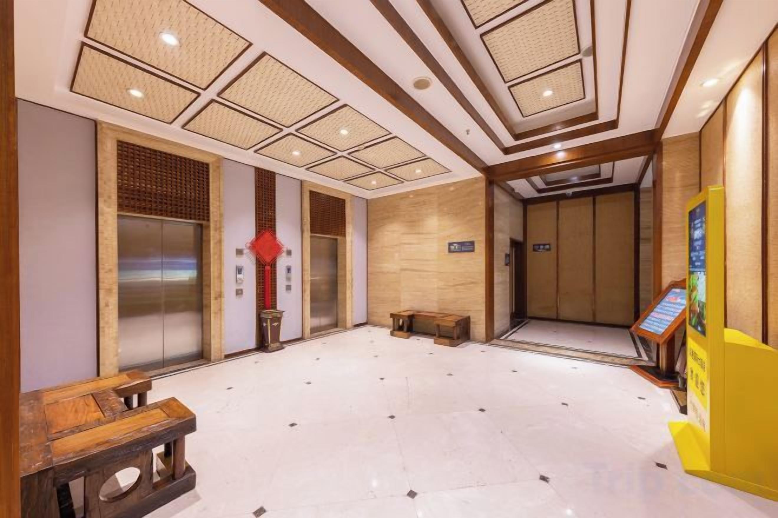 Un vestíbulo de hotel con mostrador de recepción, ascensores y un banco de madera.