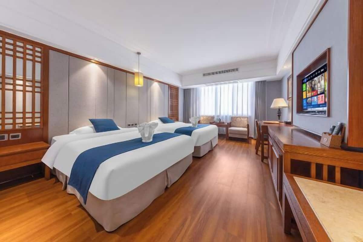 A hotel room with two beds, a wooden bench, a desk, and a TV on the wall.