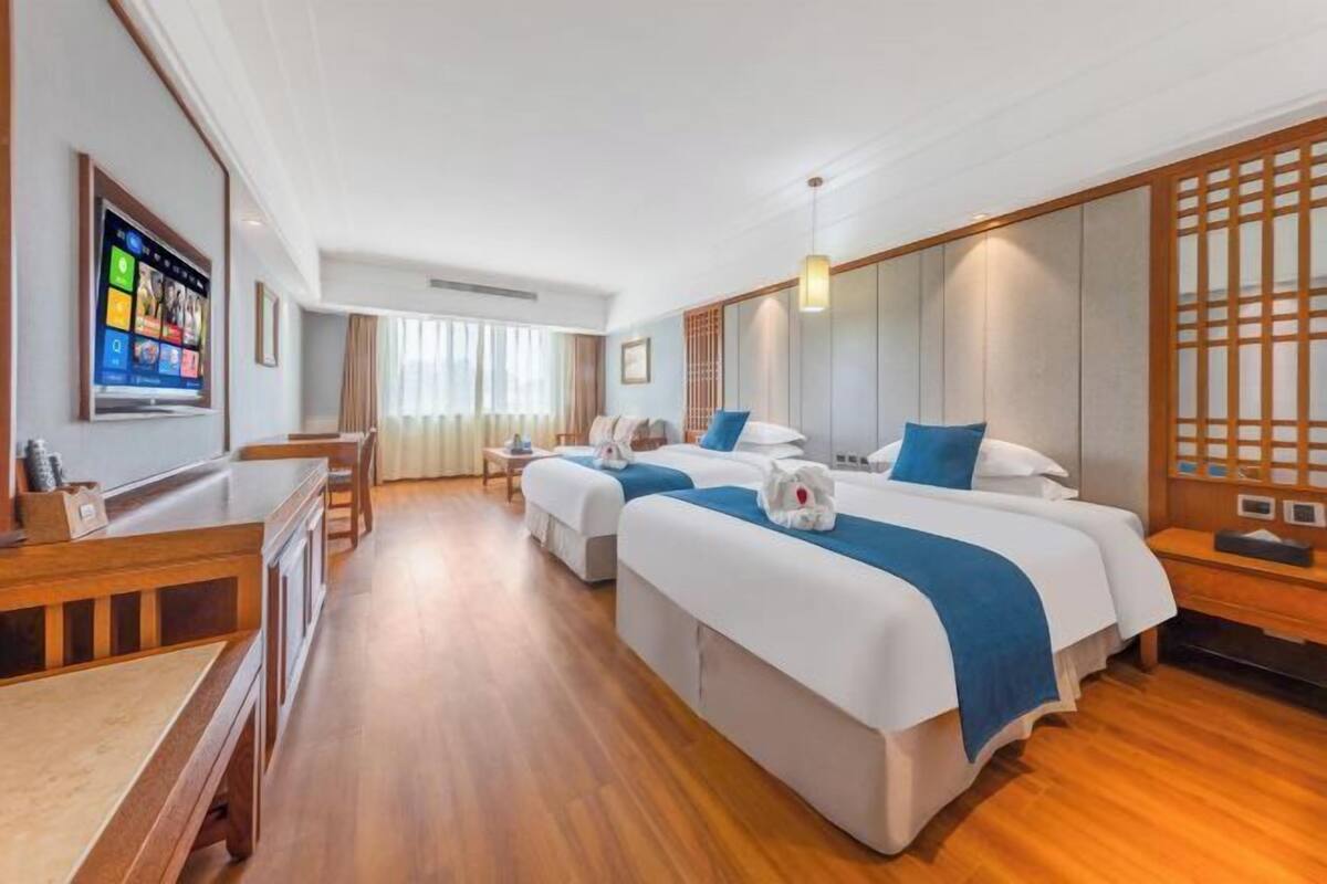 A hotel room with two beds, a desk, a chair, and a TV mounted on the wall.