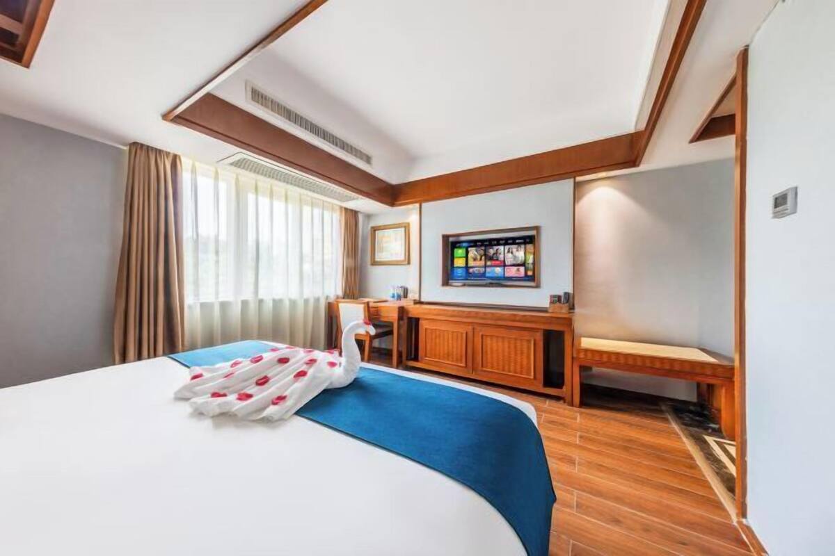 A hotel room with a bed, a desk, a television, and a window with curtains.