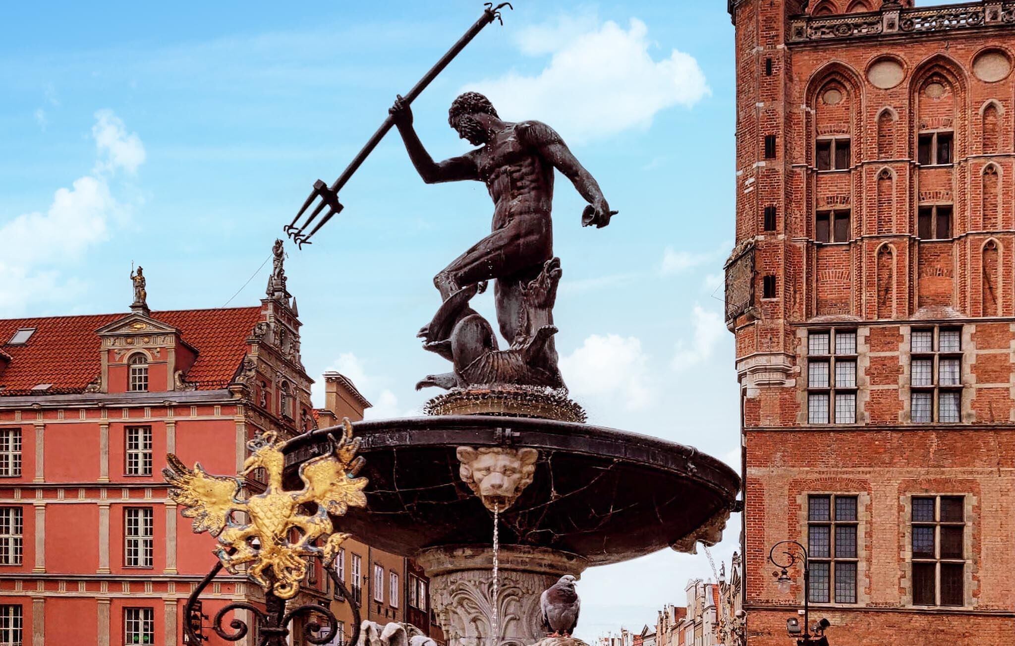A statue of a man holding a staff on a fountain, surrounded by ornate architectural buildings.