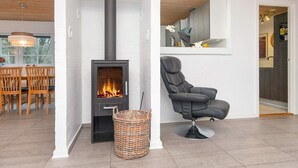 A modern living room with a wood-burning stove, a comfortable black chair, and a dining area with wooden chairs and a table. - 4 Star Holiday Home in Ulfborg (Ulfborg)