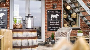 A rustic building with a brick facade, a large glass door, and a metal staircase. There are signs indicating the sale of quality dairy products. - 4 Star Holiday Home in Ulfborg (Ulfborg)