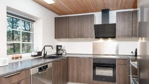 A modern kitchen with wooden cabinets, a built-in oven, and a dishwasher. - 4 Star Holiday Home in Ulfborg (Ulfborg)
