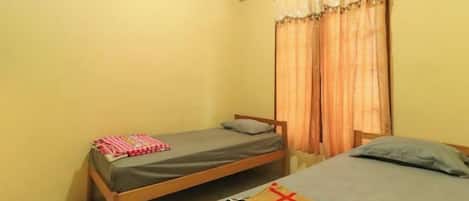 A small room with two single beds, a window with curtains, and a tiled floor.
