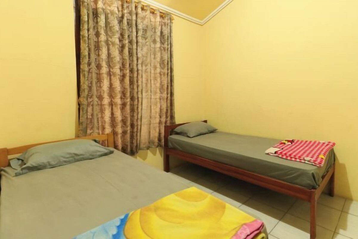 A room with two single beds, a window with curtains, and a tiled floor.