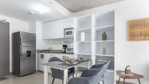 Een moderne keuken met een inbouwkoelkast, een magnetron en een koffiezetapparaat. Twee stoelen en een kleine tafel met een decoratief object.
