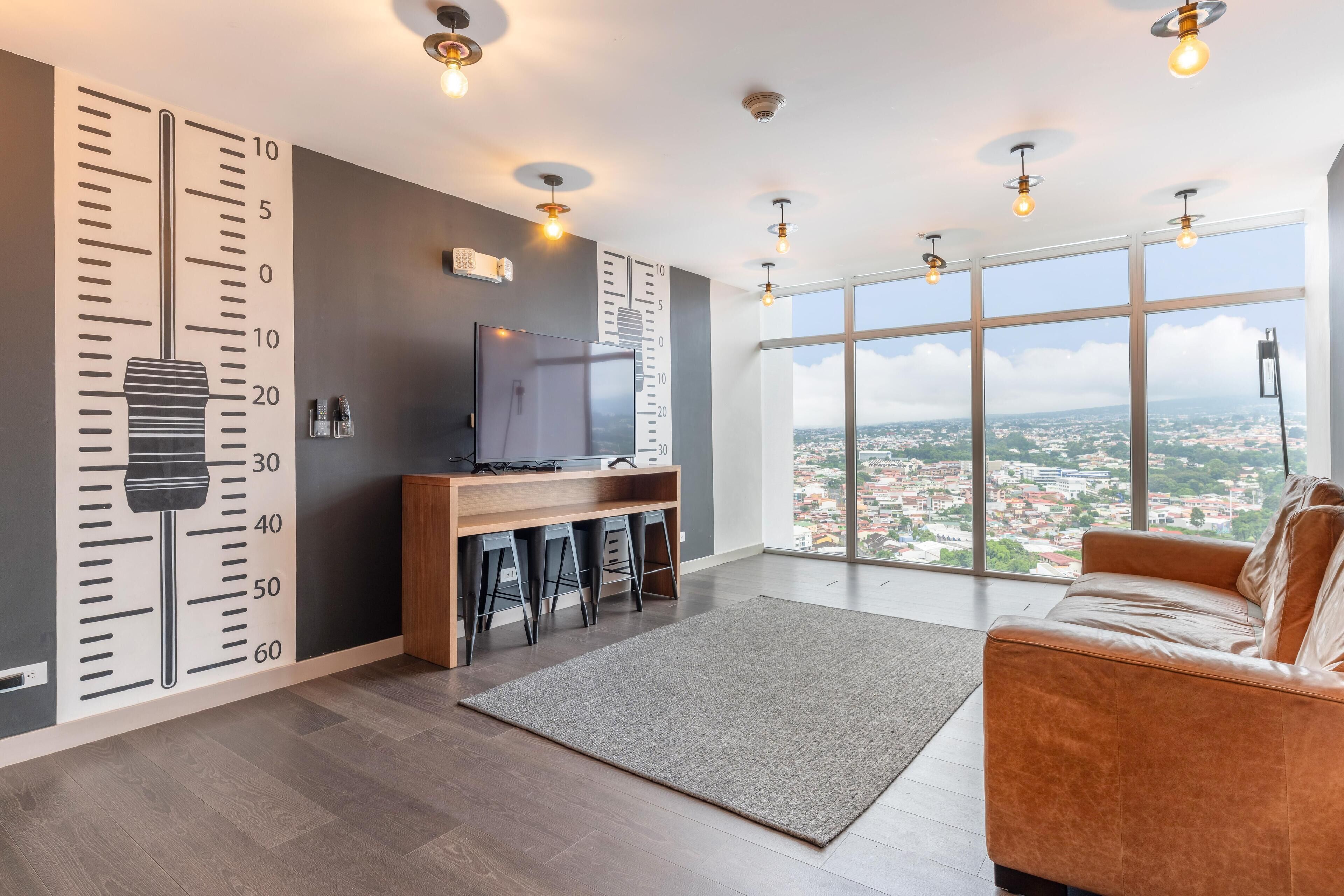 A modern living room with a large window, a TV, and a bar area.