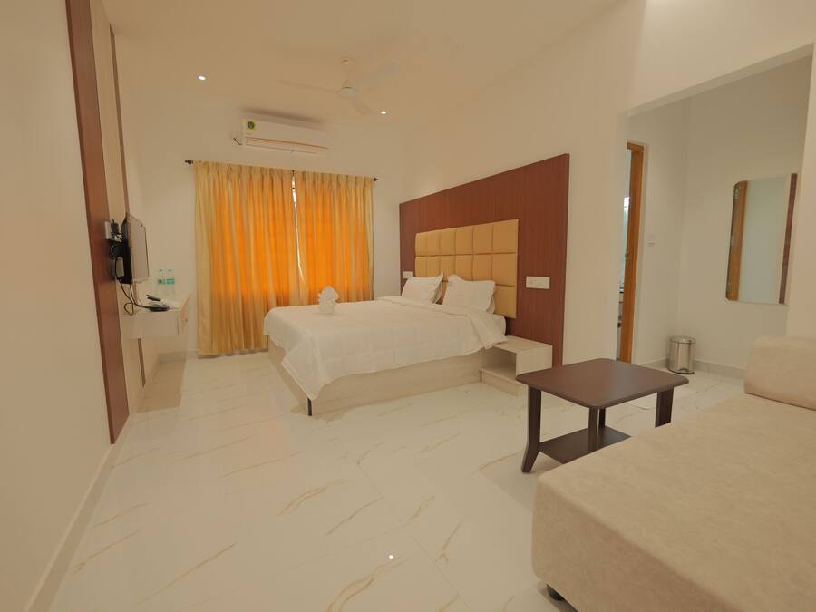Quarto de hotel com cama, sofá, mesa pequena, televisão e banheiro com espelho.
