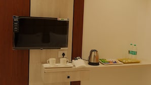 Une chambre d’hôtel équipée d’un téléviseur à écran plat, d’une machine à café, d’un plateau avec des tasses et une serviette, ainsi qu’une bouteille d’eau posée sur le comptoir.