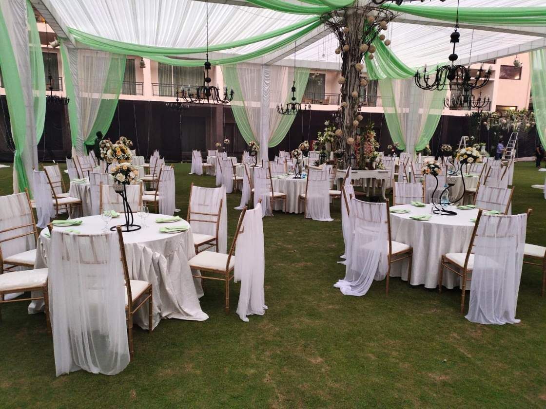 An outdoor wedding venue with round tables, white chairs, and green drapes.