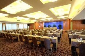 A conference room with multiple tables and chairs, a stage with a blue backdrop, and a patterned carpet. - Meiyuan Hotel (Jiashan)