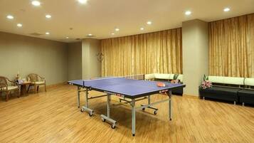 Una habitación con mesa de ping pong, piso de madera y una zona de estar con sillas y sofá.