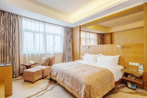 A hotel room with a large bed, a sitting area with a chair and ottoman, a bedside table, and a window with curtains. - Meiyuan Hotel (Jiashan)