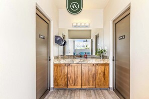 Features a central vanity with granite countertop and wooden cabinetry, a ceiling-mounted showerhead, and a mirror above.