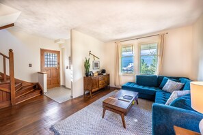 A living room with a blue sofa, wooden coffee table, and a staircase leading to another room. - Swiss Chalet with Private Deck & Mountain Views (Golden)