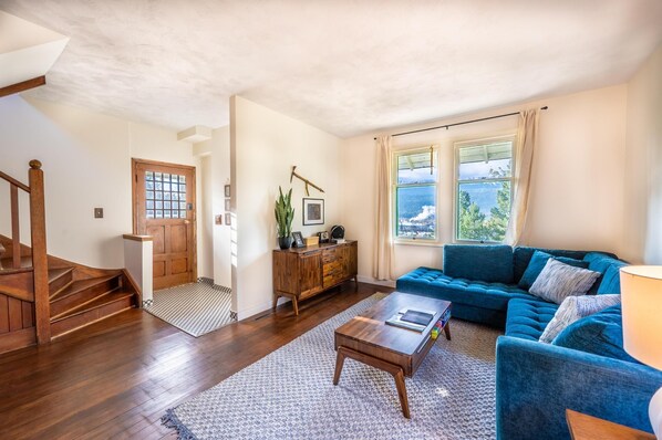 A living room with a blue sofa, wooden coffee table, and a staircase leading to another room. - Swiss Chalet with Private Deck & Mountain Views (Golden)
