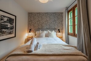 A neatly made bed with white linens and rolled towels, a patterned wallpaper, and a framed picture on the wall. - Swiss Chalet with Private Deck & Mountain Views (Golden)