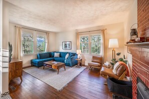 A cozy living room with a blue sectional sofa, a wooden coffee table, a leather armchair, and a fireplace. - Swiss Chalet with Private Deck & Mountain Views (Golden)