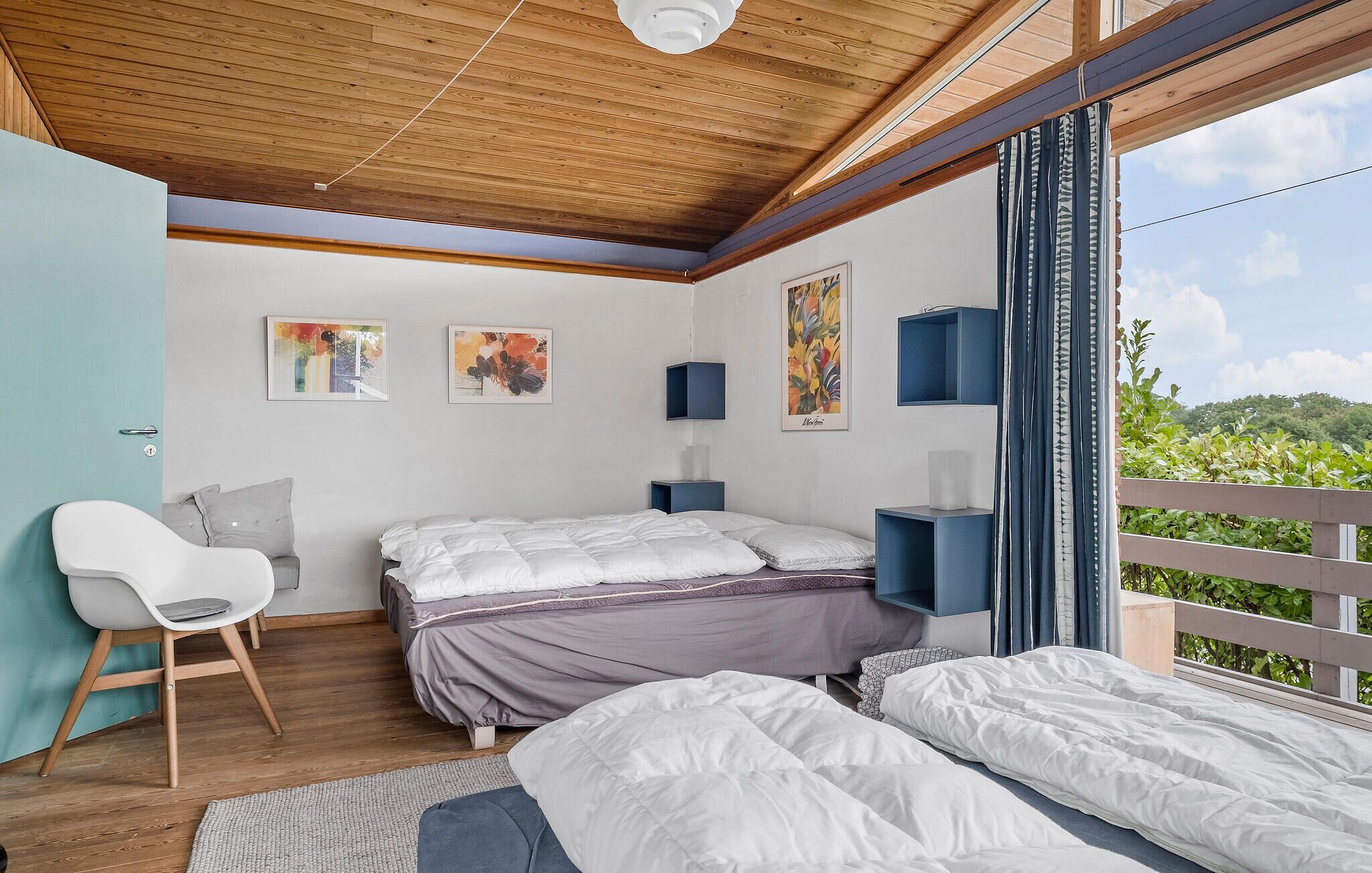 A bedroom with a wooden ceiling, a bed, a chair, and artwork on the walls.