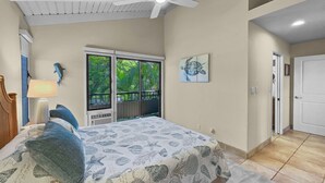 Ein Schlafzimmer mit einem Bett, einem Deckenventilator, einem Fenster mit Blick auf Grünflächen, einer Tür und einer Wand mit einem Schildkrötenbild.