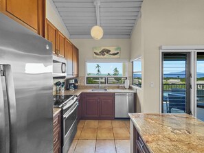 A modern kitchen with stainless steel appliances, wooden cabinets, and a view of the ocean through a window.