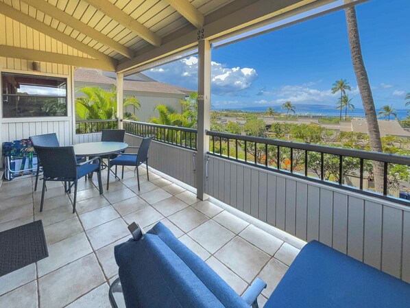 A covered outdoor area with a table and chairs, a view of the beach, and a railing.