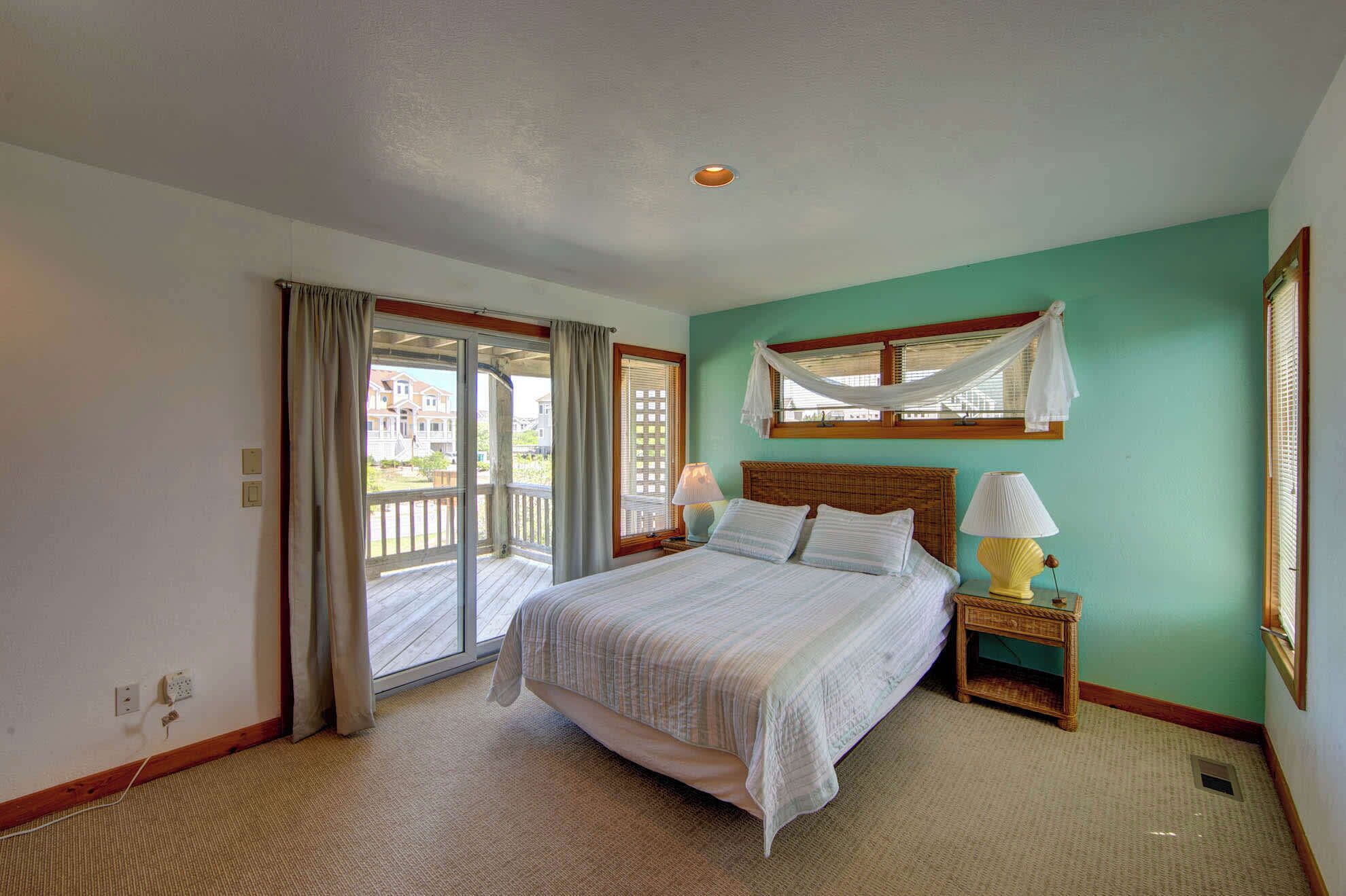 A bedroom with a bed, two bedside tables with lamps, a window with a white curtain, and a view of a building outside.