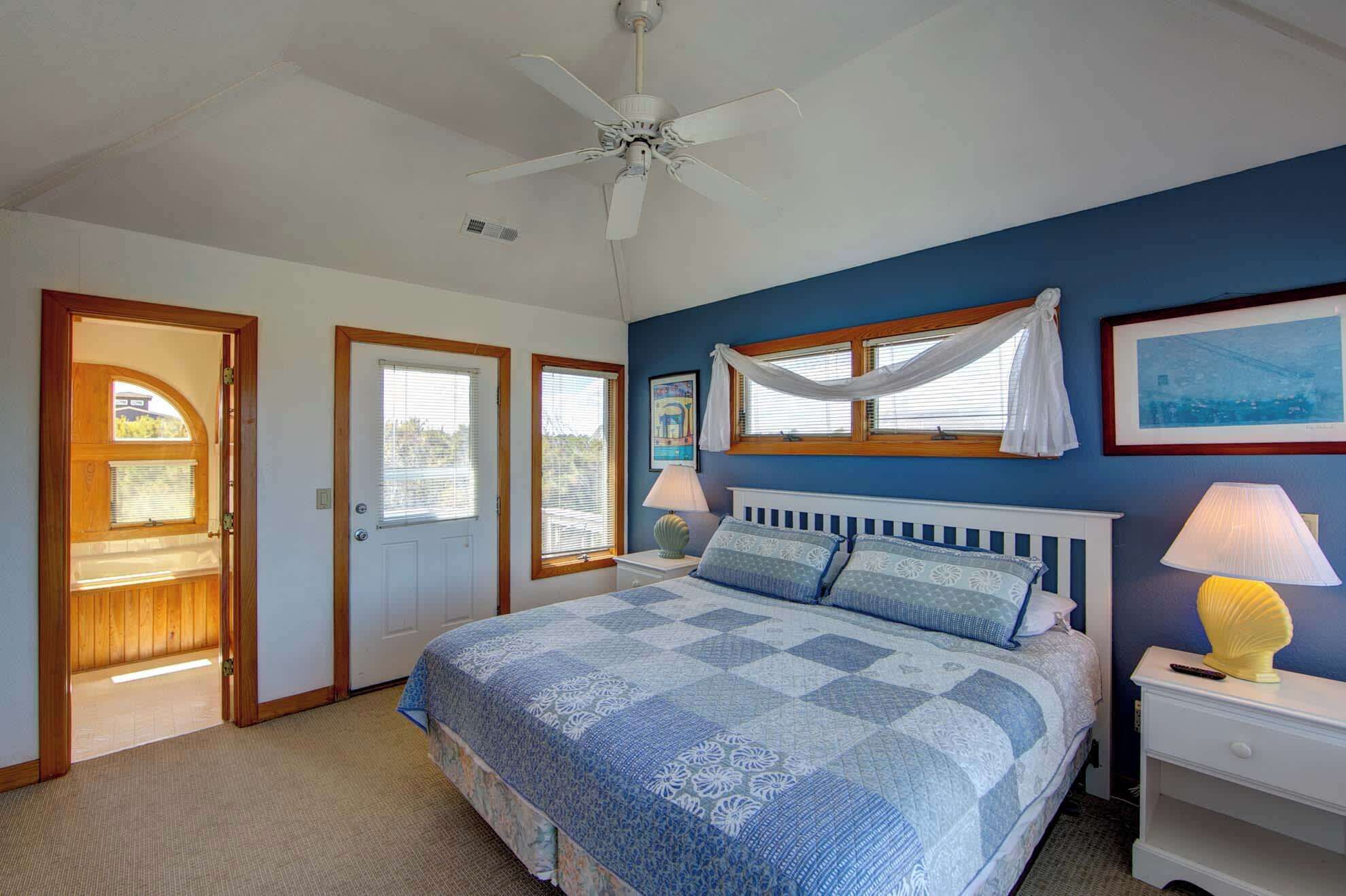 A bedroom with a bed, a ceiling fan, a window with curtains, and a nightstand with a lamp.