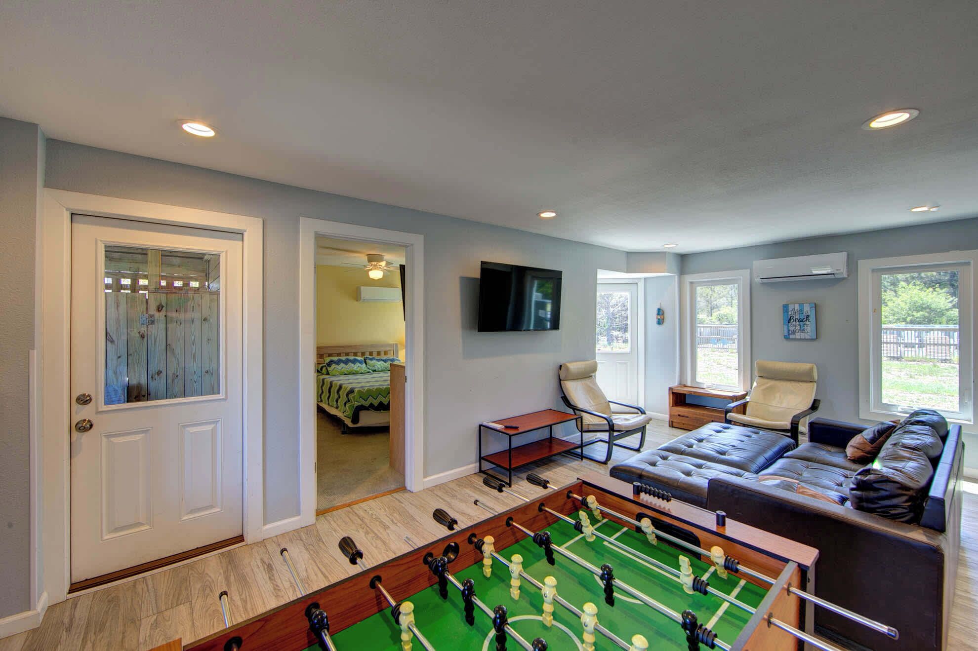 A room with a foosball table, a sofa, and a television on the wall.