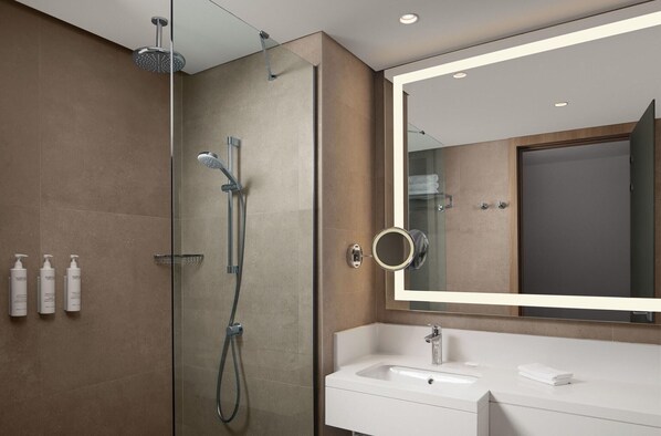 Un baño moderno con cabina de ducha de vidrio, un espejo grande y un lavamanos blanco.