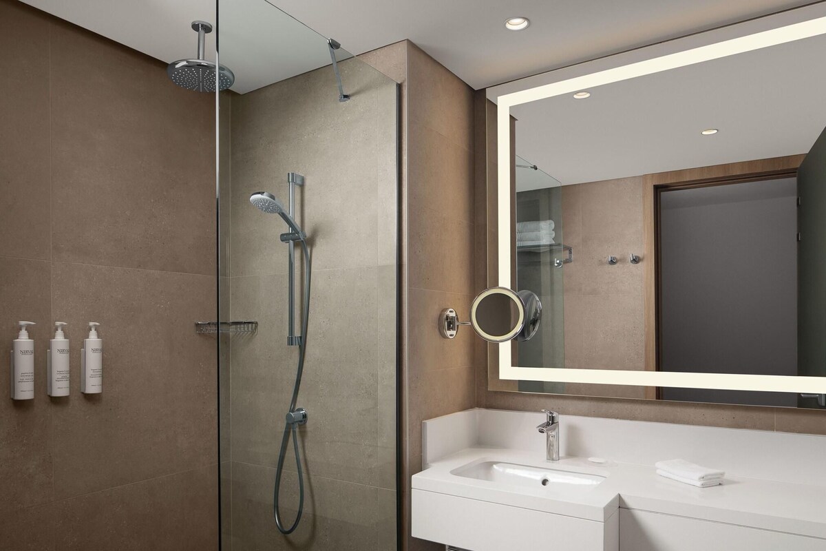 Une salle de bain moderne avec une douche à parois de verre, un grand miroir et un lavabo blanc.