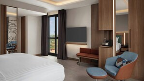 A modern hotel room with a large bed, a seating area with a sofa and armchair, a flat-screen TV mounted on the wall, and a large window with curtains. - Courtyard By Marriott Dakar Diamniadio (Diamniadio)