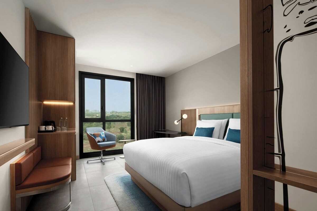 Una habitación de hotel moderna con una cama grande, una zona de estar, un escritorio y vistas al exterior.