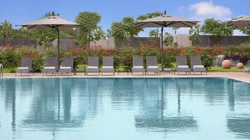 Une piscine entourée de verdure et d’une clôture, avec des chaises longues et des parasols.