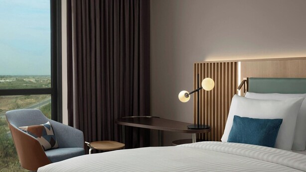 Een hotelkamer met een groot raam, een bed, een bureau, een stoel en een lamp.
