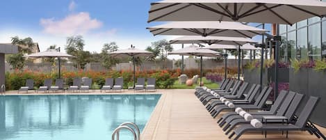 A swimming pool with lounge chairs and umbrellas, surrounded by a wooden deck and a garden with flowers.