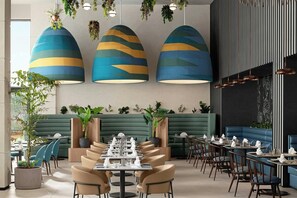 Un intérieur de restaurant moderne avec des niveaux d’assises, des plantes suspendues et un mélange d’agencements de tables et de banquettes.