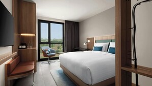 A modern hotel room with a large bed, a seating area, a desk, and a view of the outdoors. - Courtyard By Marriott Dakar Diamniadio (Diamniadio)