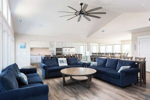 Un vaste salon doté d’un ventilateur de plafond, un coin repas avec des chaises en bois et une cuisine à l’arrière-plan.