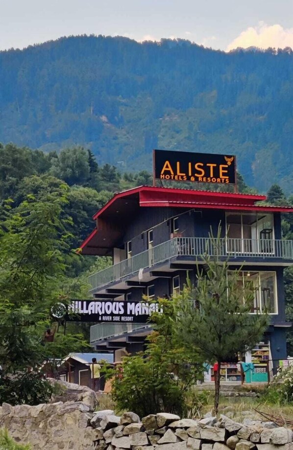 A hotel named 'Aliste Hotels & Resorts' with a signboard, a balcony, and a view of a mountainous landscape. - Aliste - A Boutique Cottages Resort (Manali)