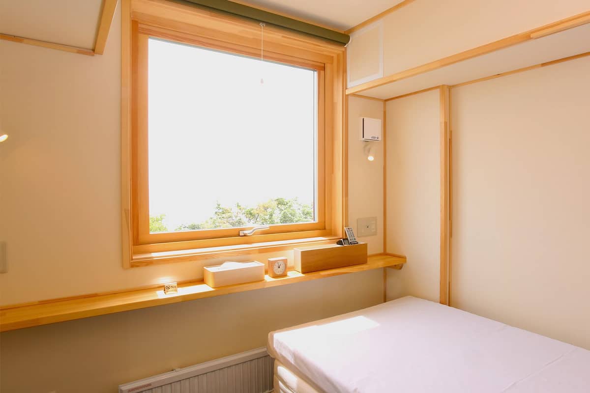 A small, bright room with a window, a bedside table, a nightstand, and a bed.