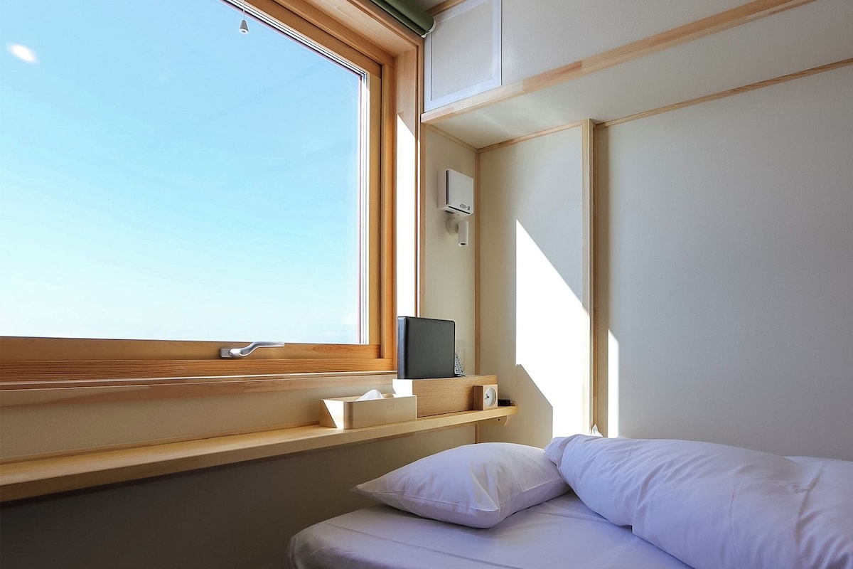 Ein Schlafzimmer mit einem Bett, einem Nachttisch, einem Fenster und einer wandmontierten Klimaanlage.