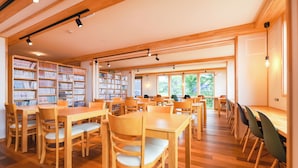 A spacious library with wooden tables and chairs, large windows, and bookshelves filled with books.