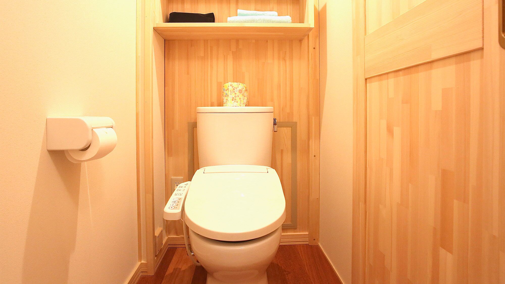 A small, narrow bathroom with a toilet, a toilet paper holder, and a shelf above the toilet.