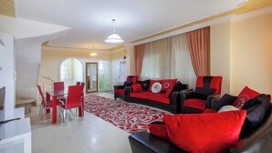 A modern living room with a red and black sofa set, a dining area with red chairs, and a patterned rug. - Avsallar Kepenek Village (Alanya)