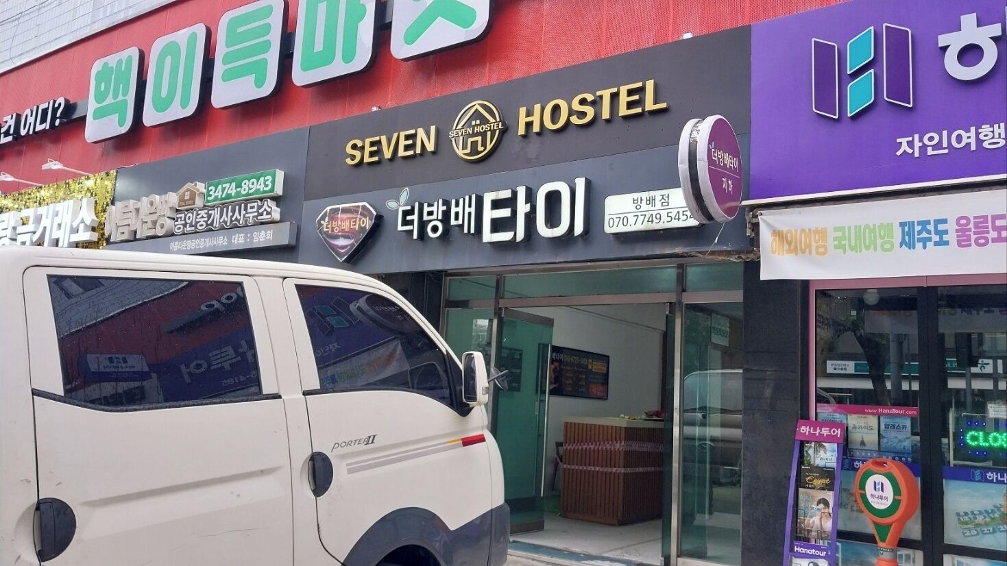 A building with a sign for 'SEVEN HOSTEL' and a 'Portez' van parked in front.