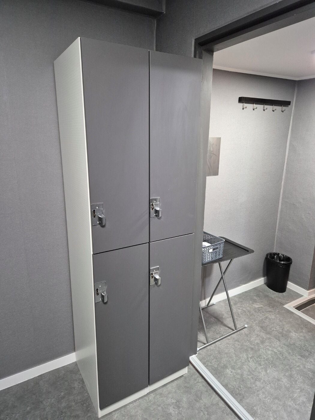 Une armoire métallique grise à deux portes et une petite table avec un panier.