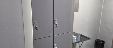 Un armario metálico gris con dos puertas y una pequeña mesa con una cesta.